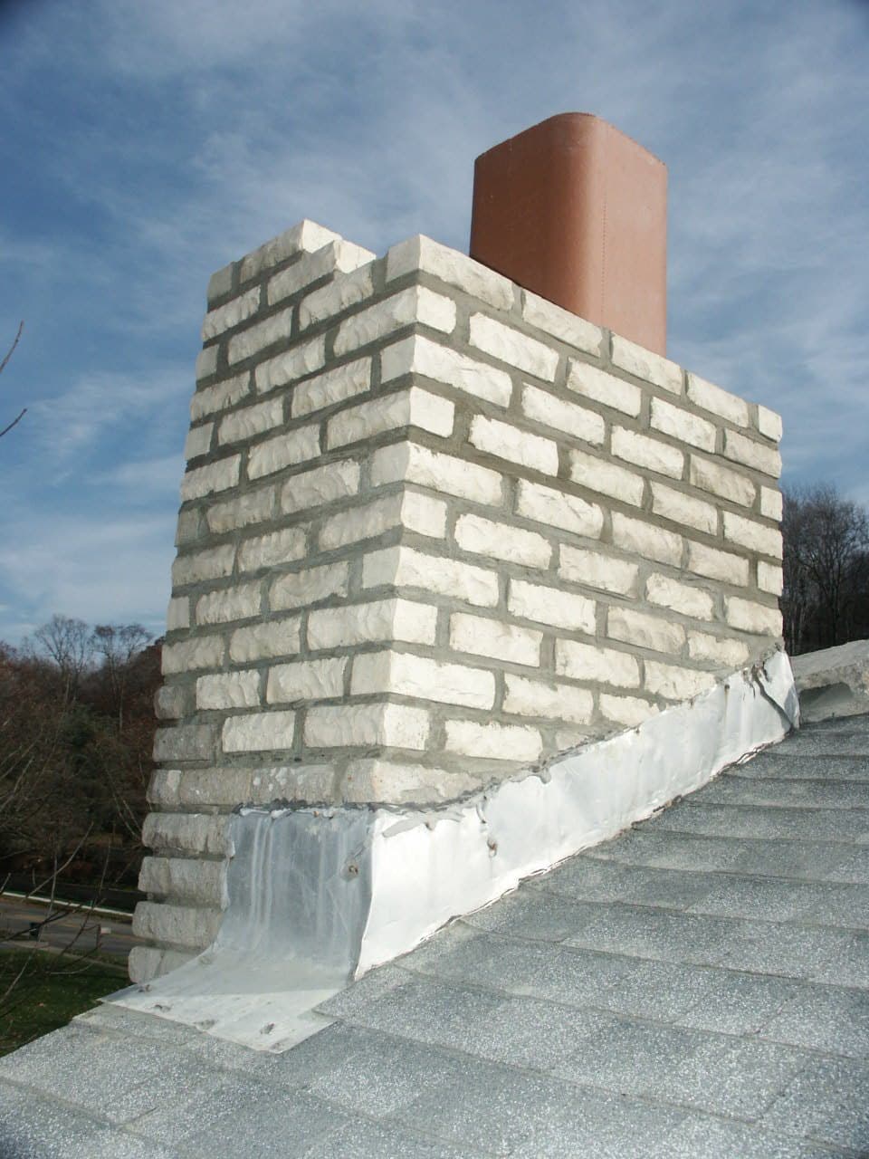 Chimney rebuilt from the flashing up in cream-colored brick with a new clay flue, against a blue sky
