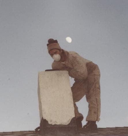 Dan on a roof wearing a dust mask, cleaning a chimney crown