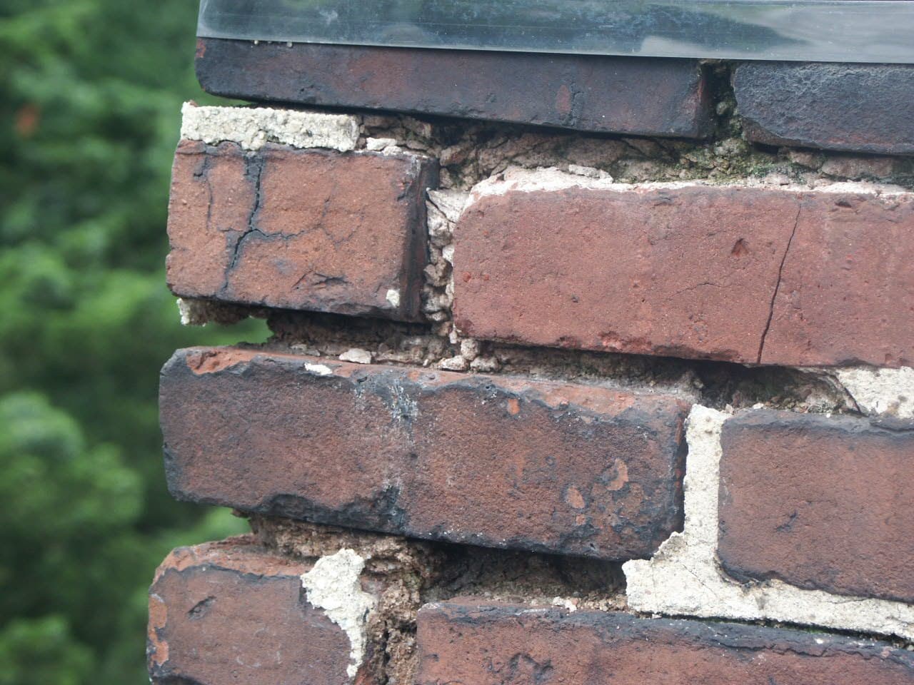 Close-up of a brick chimney showing cracked brick faces, a brick pulling loose, and washed-out mortar joints