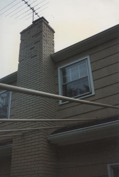 A brick chimney on a house roof whose bricks have started to shale and flake apart